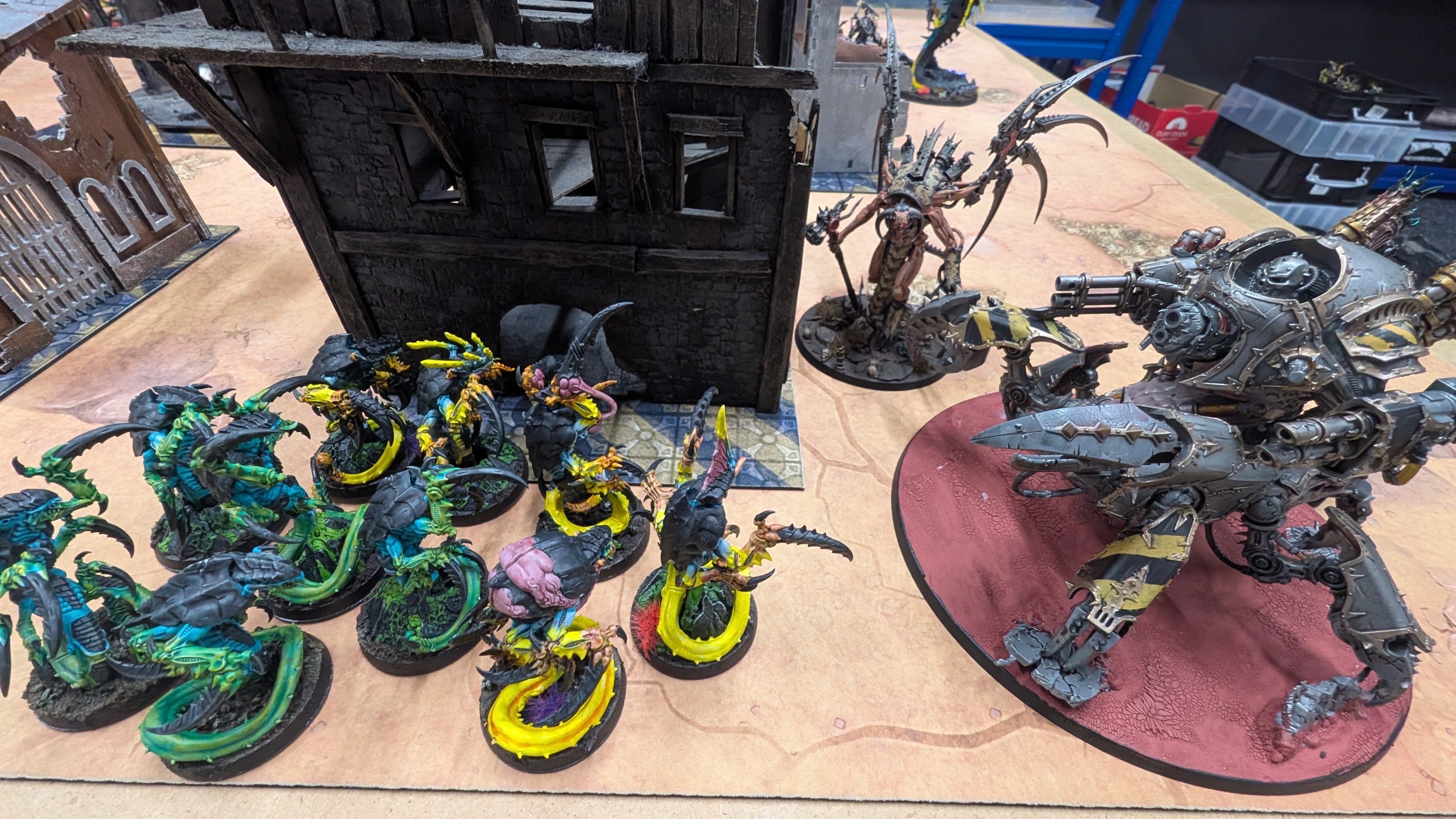 A teal and yellow Tyranid swarm faces a hazard-striped Chaos daemon engine across a ruined board