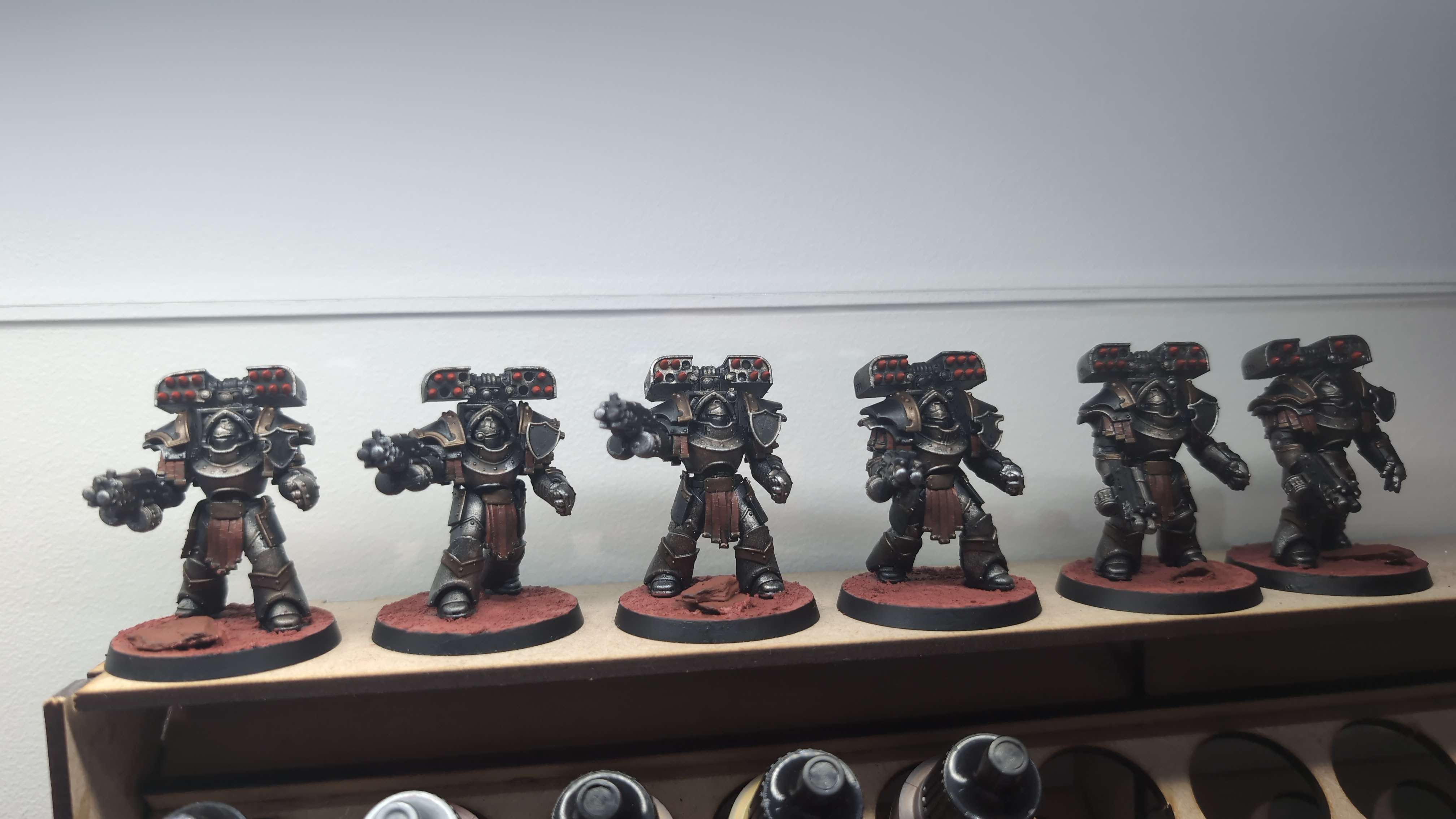 Six Iron Warriors Terminators in dark battered metal on red earth bases, lined up on a shelf