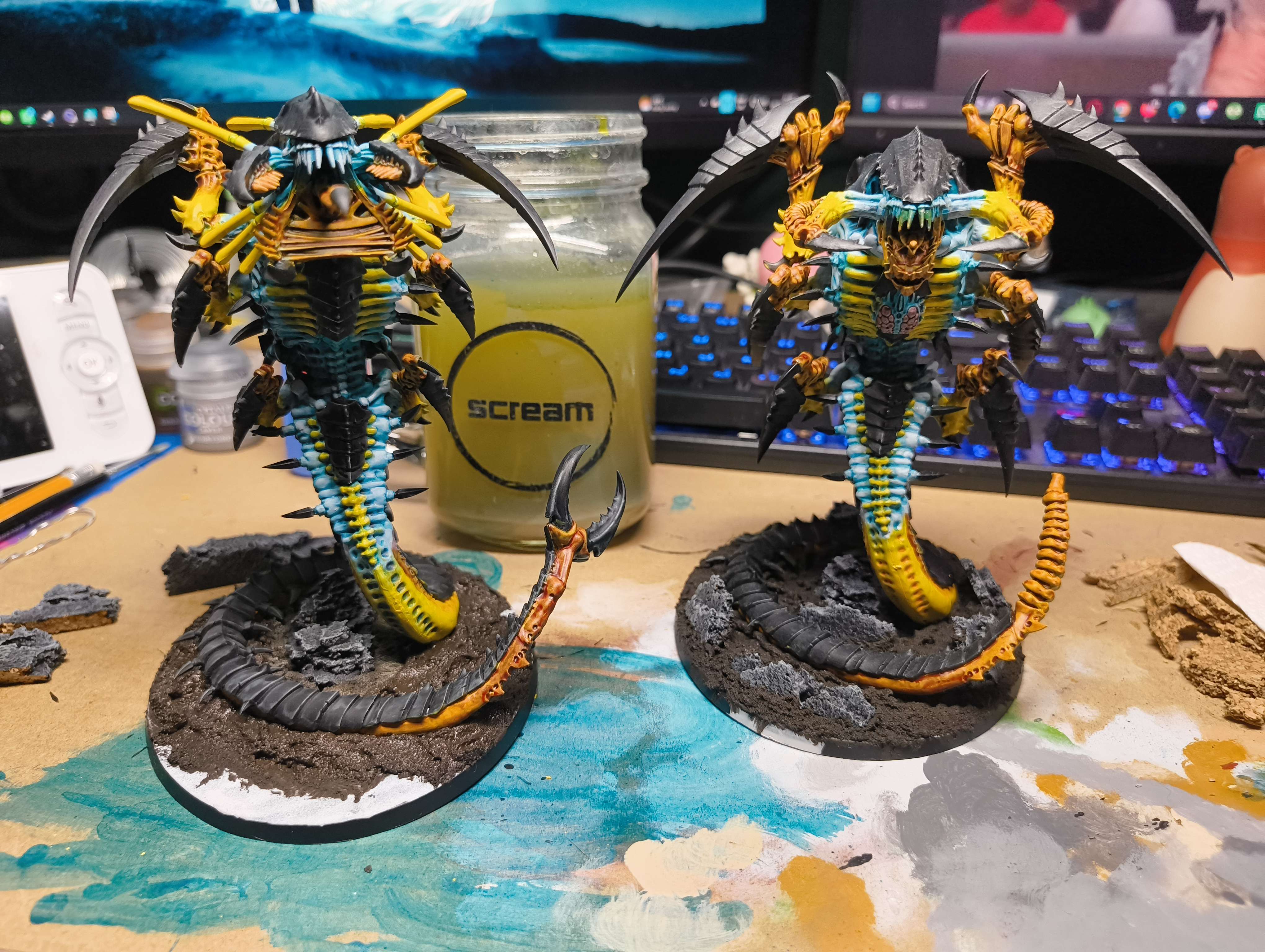 Two winged Tyranids painted in teal, yellow and bone on dark rocky bases