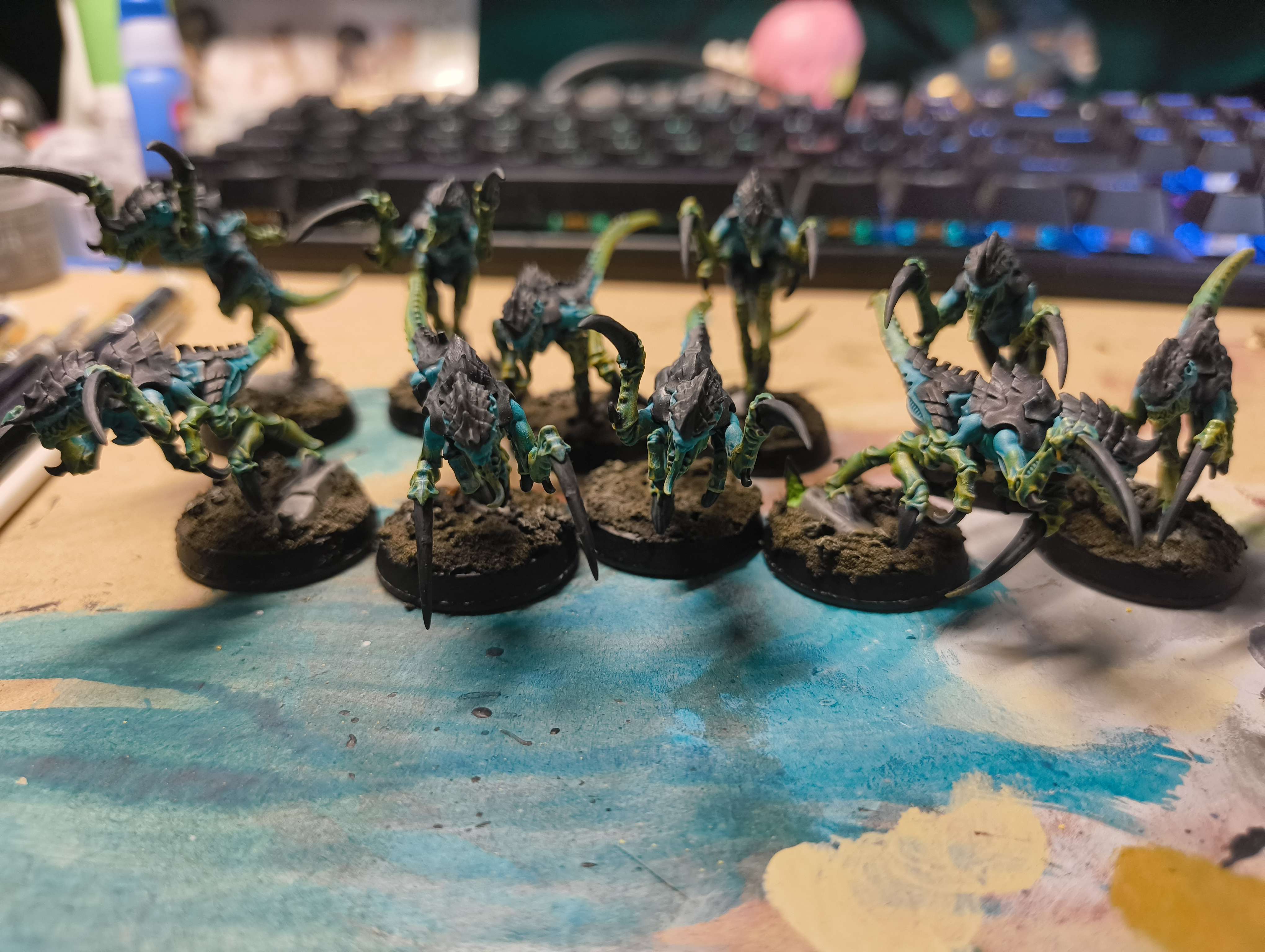 A rank of teal and grey Hormagaunts with finished earth bases on a paint-splattered mat