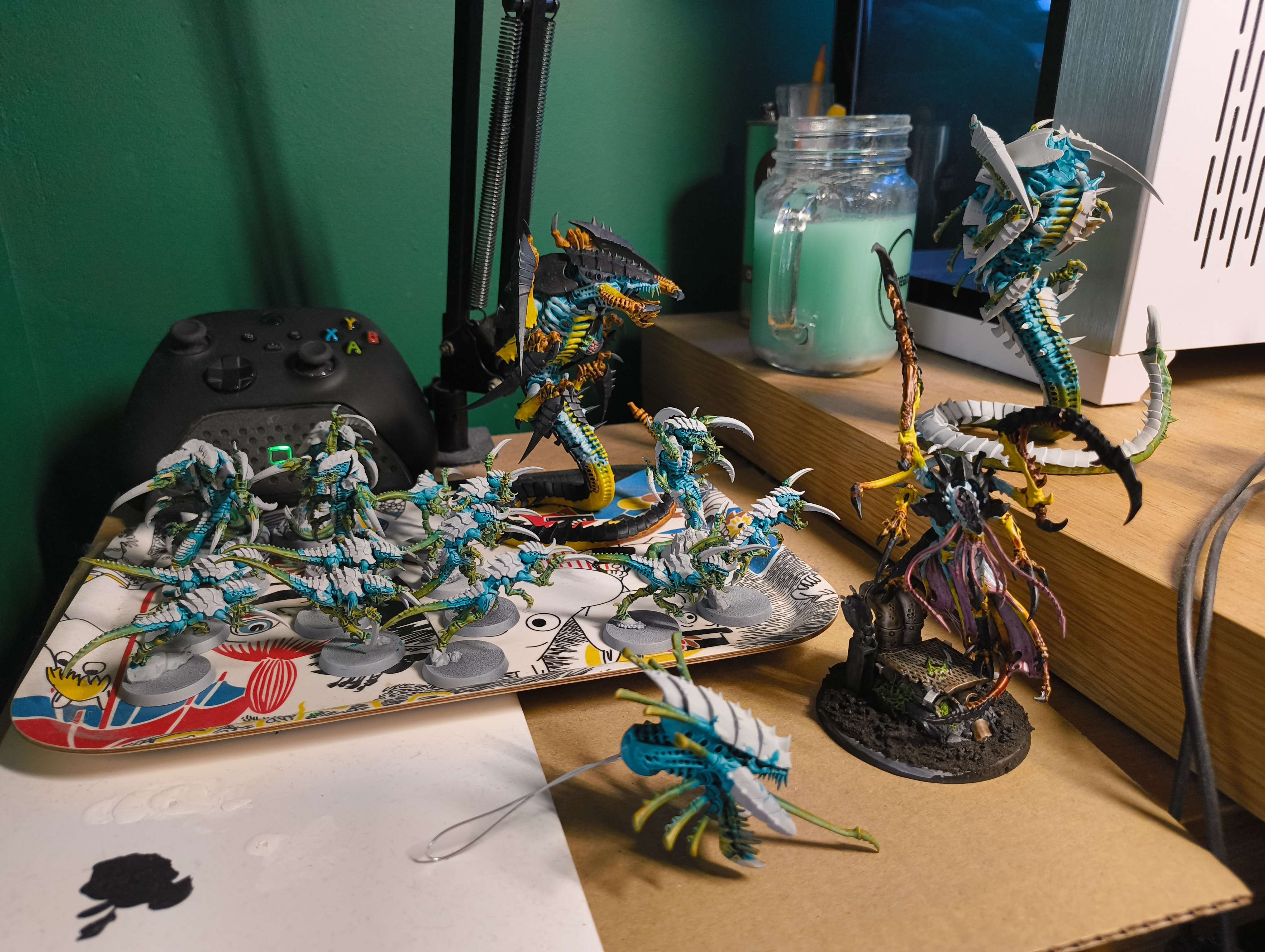 Teal and yellow Tyranid swarm arranged on a workbench, including a winged Hive Tyrant