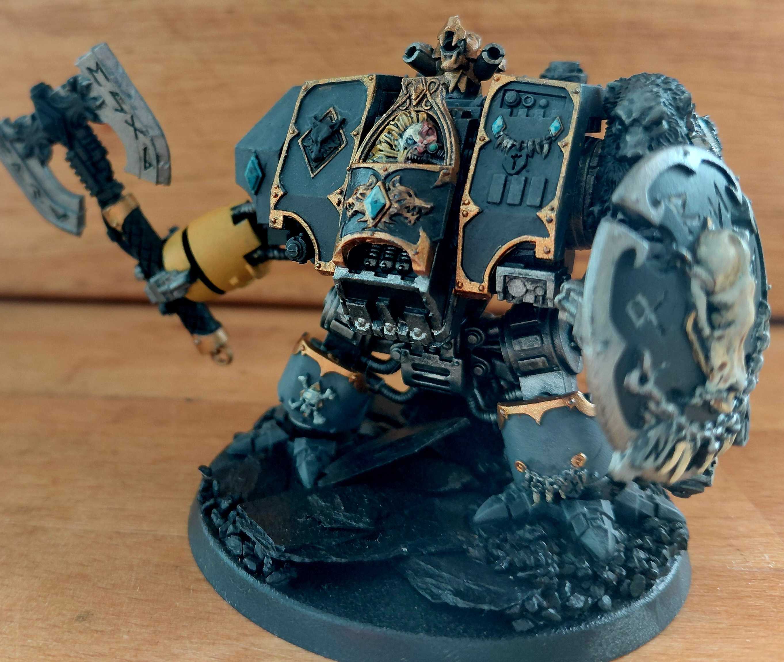 A grey and gold Space Wolves Dreadnought with a runic axe and heraldic shield on a slate base